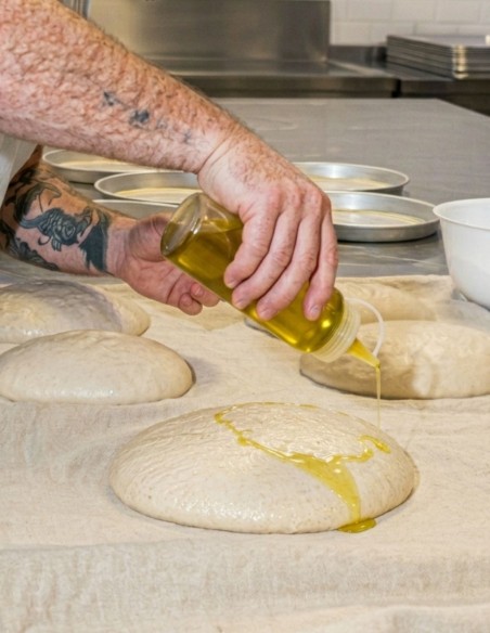 Biberón de plástico dosificando aceite sobre masa